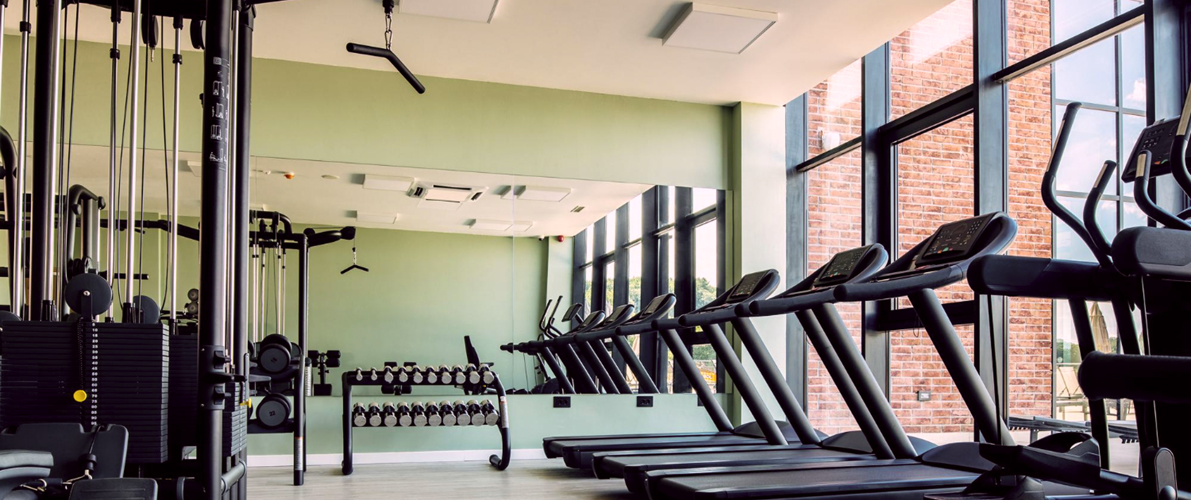 Тренажёрный зал в котом на фоне находится гантельный ряд блочный тренажёр и беговые дорожки